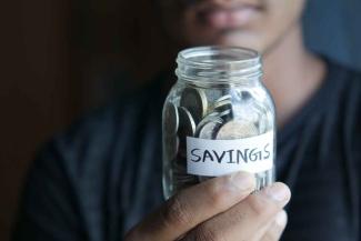 Person holding jar of coins with a 'savings' label